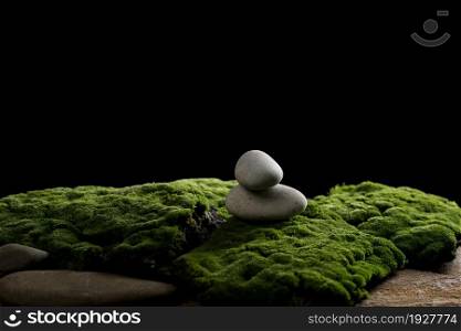stack of round stones on green moss, black background. Podium to showcase products, cosmetics and items, advertising