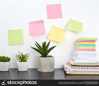 stack of spiral notebooks and colored stickers, next to a ceramic pot with a flower on a black table, white wall, Scandinavian-style minimalism