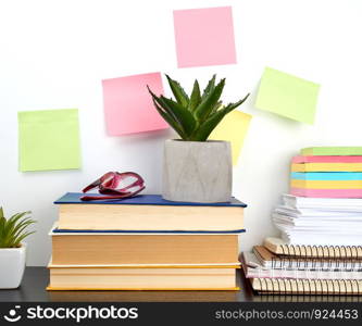stack of spiral notebooks and colored stickers, next to a ceramic pot with a flower on a black table, white wall