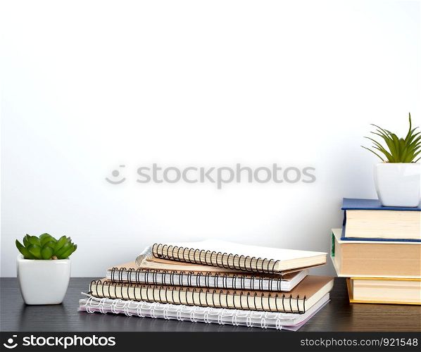 stack of spiral notebooks with white pages and ceramic pots with plants on a black table, white wall, minimalism in Scandinavian style