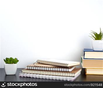 stack of spiral notebooks with white pages and ceramic pots with plants on a black table, white wall, minimalism in Scandinavian style