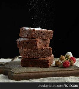 stack of square baked brownie chocolate cake slices sprinkled with white sugar, small particles fly down, low key