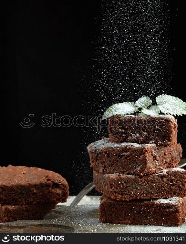 stack of square baked brownie chocolate cake slices sprinkled with white sugar, small particles fly down, low key