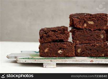 stack of square baked pieces of brownie chocolate cake with walnuts, on a wooden board, close up