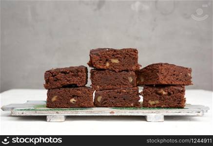 stack of square baked pieces of brownie chocolate cake with walnuts, on a wooden board
