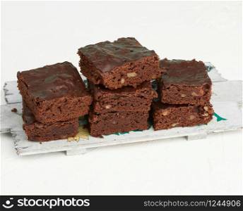 stack of square baked slices of brownie chocolate cake with walnuts on a wooden board, top view