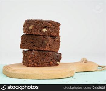stack of square baked slices of brownie chocolate cake with walnuts on a wooden board, close up
