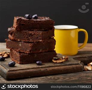 stack of square baked slices of brownie chocolate cake with walnuts on a wooden surface. Cooked homemade food. Chocolate pastry. Sweet meal, homemade dessert