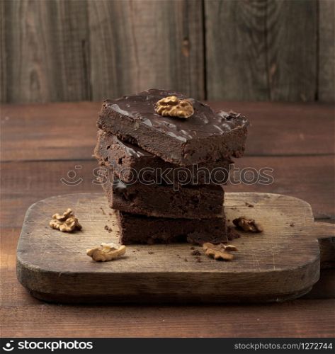 stack of square baked slices of brownie chocolate cake with walnuts on a wooden surface. Cooked homemade food. Chocolate pastry. Sweet meal, homemade dessert. Wooden table.