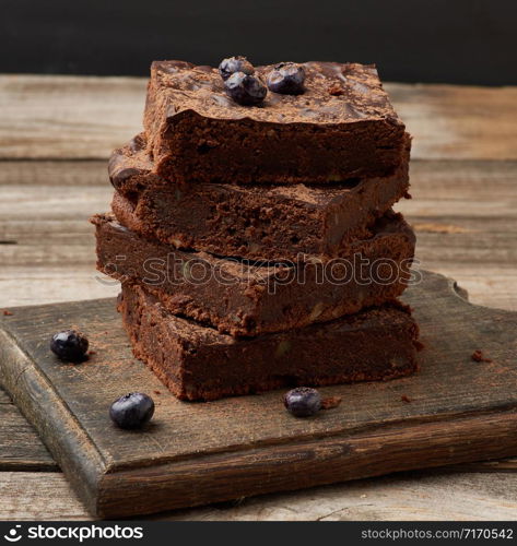 stack of square baked slices of brownie chocolate cake with walnuts on a wooden surface. Cooked homemade food. Chocolate pastry. Sweet meal, homemade dessert