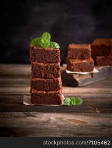 stack of square pieces of baked brownie pie on a wooden board, green mint sprig above
