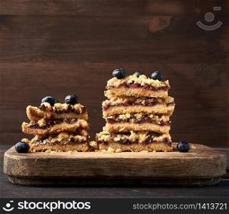 stack of square slices of baked crumble pie with blue plum on a wooden board, delicious dessert, close up