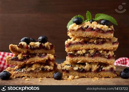 stack of square slices of baked crumble pie with blue plum on a wooden board, delicious dessert