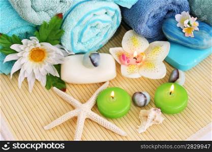 Stack of towels, soaps, candles, stones, flowers on mat background.
