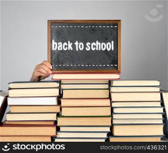 stack of various hardcover books and wooden brown chalk frame, gray background, back to school concept
