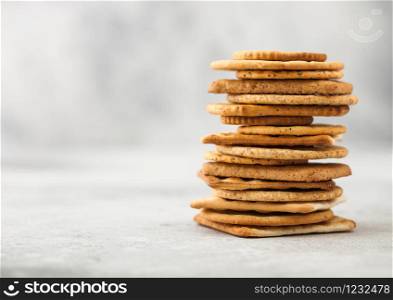 Stack of various organic crispy wheat, rye and corn flatbread crackers with sesame and salt on light background.