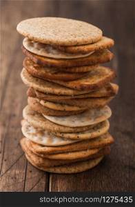 Stack of various organic crispy wheat, rye and corn flatbread crackers with sesame and salt on wood background.