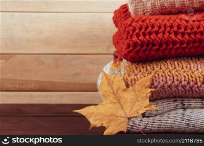 Stack of warm knitted sweaters. Autumn concept. Woolen jumpers and maple leaf on a wooden background.. Stack of warm knitted sweaters. Autumn concept. Woolen jumpers and maple leaf on wooden background.
