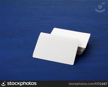 stack of white blank paper rectangular business cards on blue wooden background, template for designer