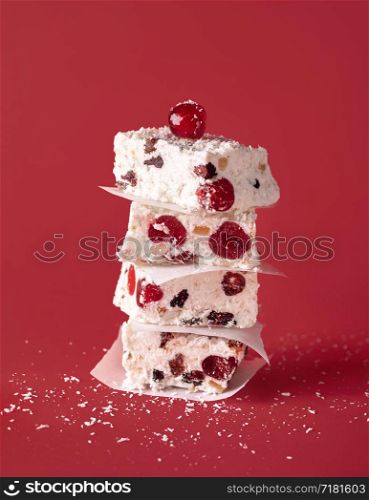Stack of white Christmas cake on a red background. Australian dried fruit cake with coconut and cherries. Xmas dessert pieces piled in a tower.