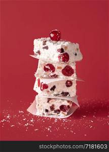 Stack of white Christmas cake on a red background. Australian dried fruit cake with coconut and cherries. Xmas dessert pieces piled in a tower.