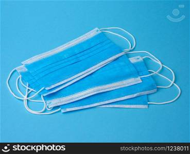 stack of white medical textile individual masks with elastic bands for protection against virus and bacteria on a blue background