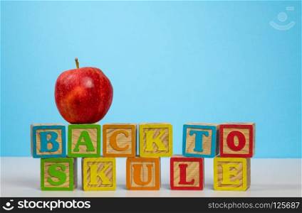 Stack of wooden blocks wrongly spelling Back to School with red apple on top against blue background. Back to School spelled wrongly with apple