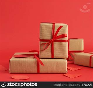 stack of wrapped gifts in brown craft paper and tied with a red ribbon on red, surprise and a gift for Valentine&rsquo;s Day February 14