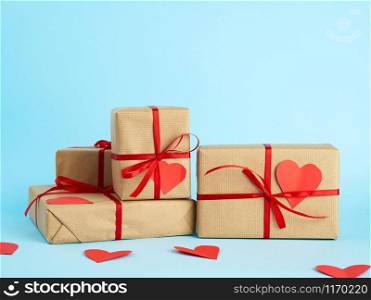 stack of wrapped gifts in brown kraft paper and tied with a red ribbon on a blue background, surprise and a gift for Valentine&rsquo;s Day February 14