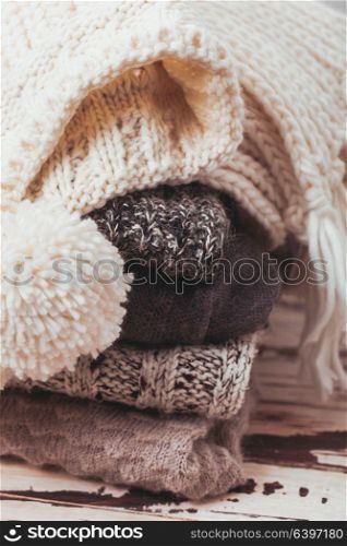 Stack warm knitted sweaters, scarf and hat in white and gray shades. Collection of woolen clothes