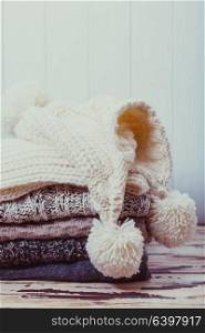 Stack warm knitted sweaters, scarf and hat in white and gray shades. Collection of woolen clothes