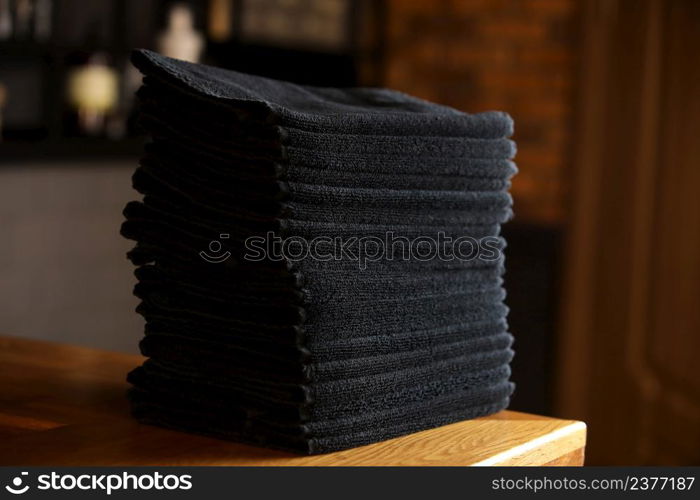 stacked black bathroom towels on a wooden table and brick wall background. spa salon, barbershop. stacked black bathroom towels on a wooden table and brick wall background. spa salon, barbershop.