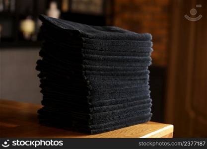 stacked black bathroom towels on a wooden table and brick wall background. spa salon, barbershop. stacked black bathroom towels on a wooden table and brick wall background. spa salon, barbershop.