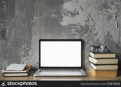 stacked books spectacles laptop with blank white screen wooden surface