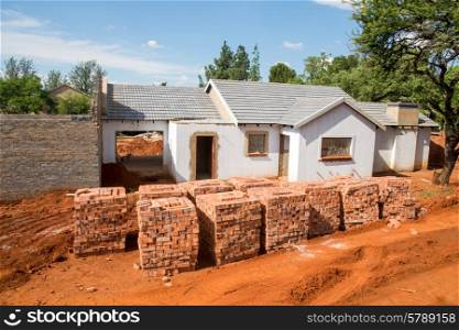 Stacked bricks in front of an incomplete house.