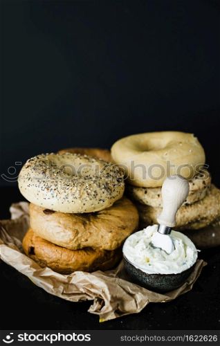 stacked different type bagel with cheese bowl against black backdrop