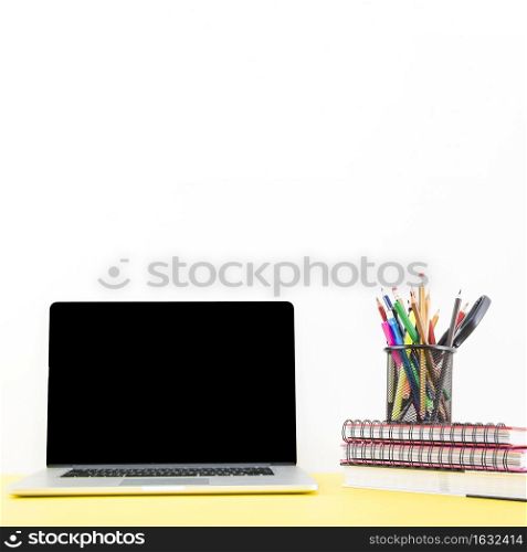 stacked notebook with various pens pencils holder near laptop desk
