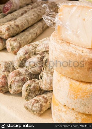 stacked rounded cheese and group of salami on tablecloth for sale in the local market