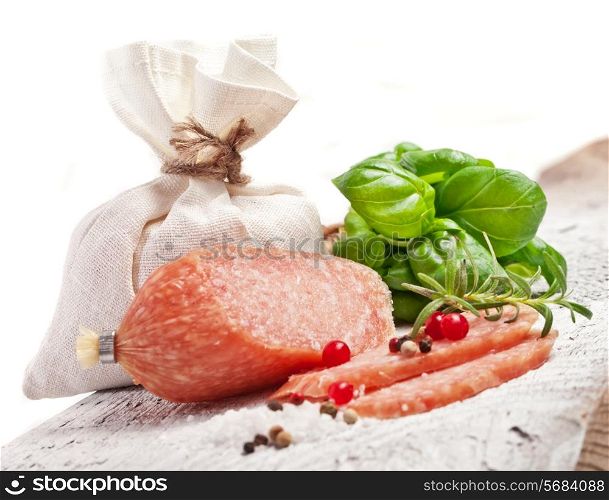Stacked sliced salami with spices on white wooden table