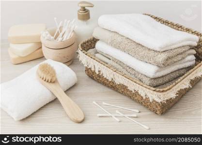 stacked towels brush soap cotton swab cosmetic bottle wooden background