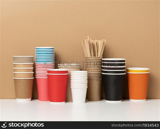 stacks of assorted disposable paper cups for drinks, coffee and tea on a white table. Takeaway beverage container