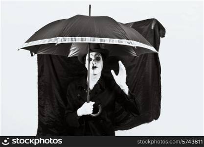 Stage actor with makeup mime in a hat holding an umbrella in his hand
