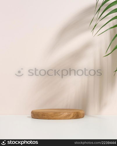 stage for displaying products, cosmetics with a round wooden podium and a green palm leaf. Shadow on the background