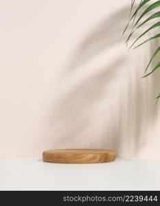 stage for displaying products, cosmetics with a round wooden podium and a green palm leaf. Shadow on the background