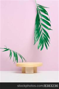 Stage for displaying products, cosmetics with a round wooden podium and a palm leaf. Pink paper background, copy space