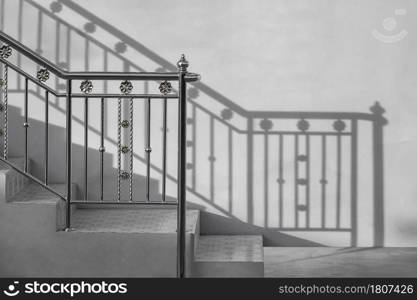 Stainless steel handrail of vintage outdoor staircase with sunlight and shadow on cement wall in black and white style