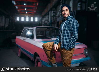 Stalker, alone traveler pose against USSR retro car, old factory interior on background. Danger zone, mysterious adventure in deserted place. Stalker, traveler pose against USSR retro car