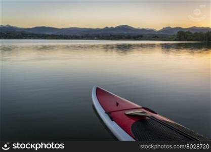 stand up paddleboard with a paddle on calm lake at dusk with Rocky Mountains in background