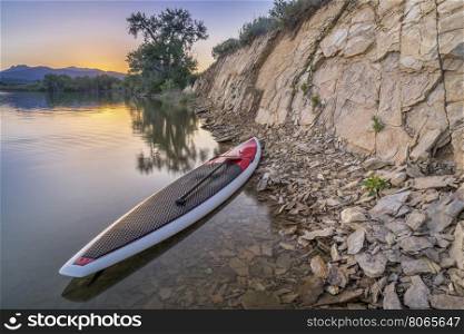 stand up paddleboard with a paddle on calm lake with a rocky cliff at dusk in northern Colorado