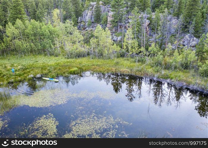 stand up paddleboard with dog and a paddler on a shore of a small lake in Rocky Mountains, late summer aerial view, vacation and recreation concept